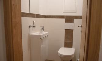 A modern bathroom with a toilet and a sink. The walls are tiled in light colors, and a wooden frame surrounds the door.