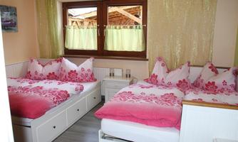 A cozy bedroom with two beds decorated with colorful bedding and pillows. The room has large windows that let in plenty of daylight.