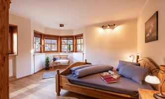 A cozy bedroom with a wooden bed and soft pillows. Large windows let in plenty of light and create an inviting atmosphere.