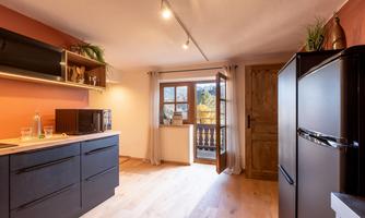 A modern kitchen with black cabinets and a large window. The room has a warm tone and plenty of daylight.