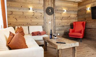 A cozy living room with wood paneling and a comfortable white sofa. The room is furnished in a modern style with a red armchair and a wooden table.