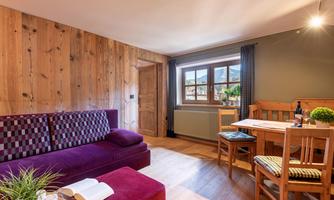 A cozy living room with a purple couch and wooden walls. A dining table and chairs complete the space, which feels inviting.