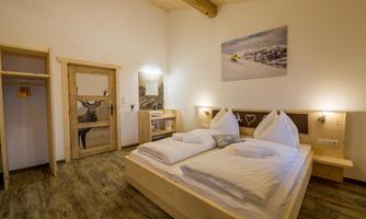 A cozy bedroom with a double bed and modern wooden accents. The walls are painted light, and a picture of a mountain landscape hangs above.