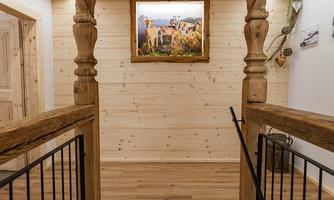 An inviting hallway with wooden paneling and a beautiful staircase. A picture hangs on the wall depicting the rural surroundings.