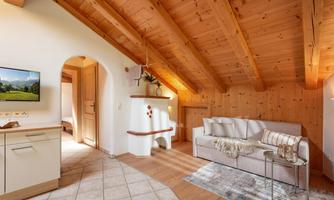 A cozy living room with a wooden ceiling and a modern sofa. A TV on the wall and a bright, inviting atmosphere.