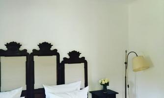 A cozy bedroom with a double bed and a wooden headboard. Next to the bed is a bedside table with a lamp and flowers.