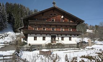 A traditional wooden house in the snow, surrounded by trees. The clear sky and the wintry landscape give the scene a tranquil atmosphere.