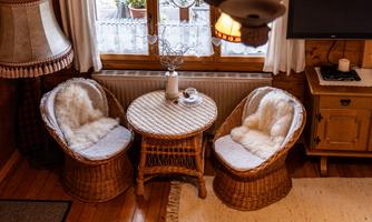 A cozy room with two wicker chairs and a small table.  
On the table, there is a flower and a candle, surrounded by a warm, wooden ambiance.