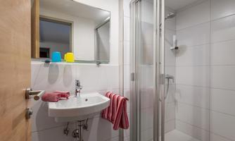 A modern bathroom with a shower and a sink. There are towels and colorful cups on the shelf.