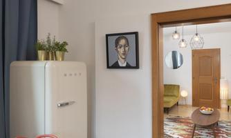 A modern living room with a refrigerator and a piece of artwork on the wall. The room is bright and cheerfully designed, with a cozy seating area.