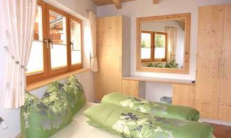 A cozy bedroom with a double bed and green pillows. There are large windows and a mirror that provide plenty of daylight.