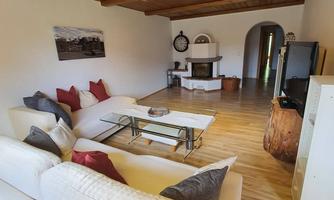 A cozy living room with a bright sofa group and a modern table. In the background, there is a fireplace and access to another room.