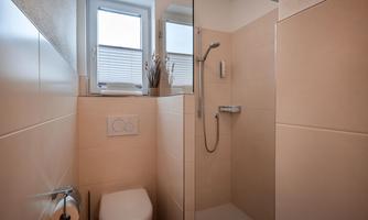 A modern bathroom with a shower and toilet. Bright tiles and windows ensure a friendly atmosphere.