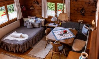 A cozy room with wooden walls and large windows.  
There is a bed, a dining area with a table and chairs, as well as a warmly decorated atmosphere.