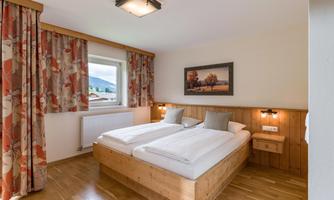A bright bedroom with two single beds and wooden furniture. Large windows and stylish curtains create an inviting atmosphere.