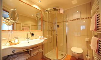 A modern bathroom with a glass shower and a large mirror. The walls are tiled beige, and towels are neatly hanging ready.