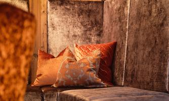 A cozy seating area with soft, light brown fabric and decorative pillows in warm colors. The walls are made of wood, creating a calm atmosphere.