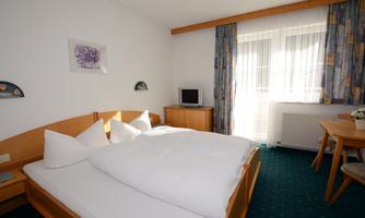 A cozy bedroom with a double bed and bright, cozy furniture. A window lets in plenty of light, and there is a small table with chairs.