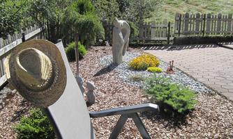 A comfortable lounge chair in the garden with a straw hat. In the background, trees and a hill are visible.