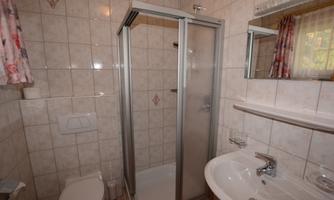 A small bathroom with a shower, a sink, and a toilet. The walls are tiled with light tiles.