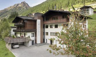 A modern building in a picturesque mountain landscape. The surroundings are green and hilly, with mountains in the background.