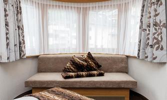 A cozy living area with a sofa and decorative cushions. Large windows let in plenty of light and create a bright atmosphere.
