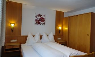 A cozy bedroom with a double bed and wood-clad walls. There is a floral painting on the wall and two nightlights.