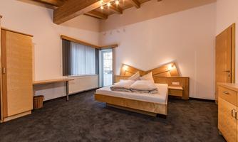 A modern bedroom with wooden ceilings and carpet flooring. The room features a double bed and a desk with a window.