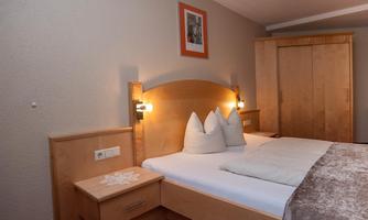 A cozy bedroom with a large bed and wooden furniture. The walls are light, and there is a stylish wall decoration.