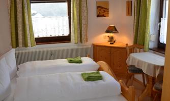 A cozy bedroom with a double bed and bright curtains. The room features a small table and a sink.