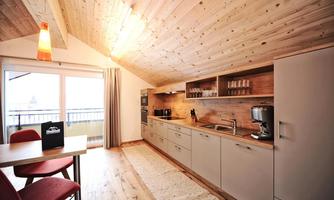 A modern kitchen nook with wooden walls and a large window front. The space is bright and inviting, with a table and chairs in warm colors.