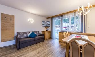A modern living room with a cozy sofa and a dining table. Large windows let in plenty of light and provide a view outside.