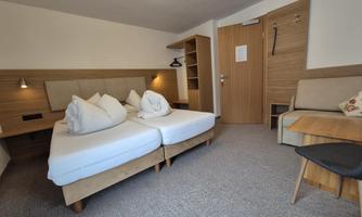 A cozy hotel room with two single beds and modern wooden interior. There are practical shelves and a desk on the wall.