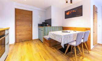 A modern kitchen with a dining area. The space is bright and friendly, with wooden floors and a cozy seating area.