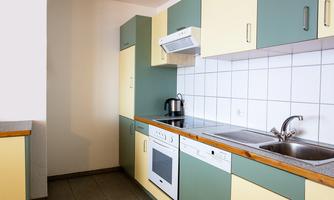 A modern kitchen with green and yellow cabinets. There is a sink, a stove, and a window for natural light.