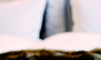 An elegant bedroom with white pillows and a warm blanket. In the foreground lies a decorative book.