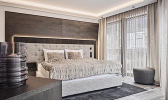 A modern bedroom with a large bed and a cozy bedspread. Plenty of daylight streams through the windows, which are adorned with elegant curtains.