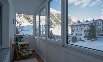 A sunny balcony with a view of snow-covered mountains and a peaceful environment. Comfortable loungers are in the foreground.