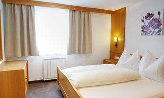 A cozy room with a double bed and light curtains. The walls are in neutral colors, and a decorative picture complements the decor.