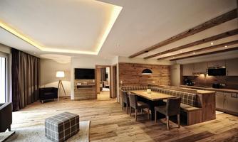A modern living room with wood decor and a large dining table. There is a cozy seating area and plenty of daylight.