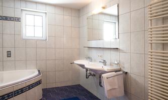 A modern bathroom with a bathtub and two sinks. The walls are tiled and there is a large window for natural light.