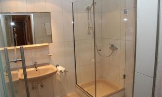 A modern bathroom with a shower and a sink. The walls are tiled in light colors, and there is a large mirror.