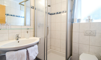 A modern bathroom with a shower and sink. White tiles and a bright window create a friendly atmosphere.