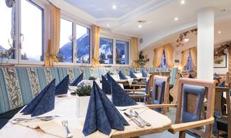 An inviting restaurant with wooden chairs and tablecloths. The windows offer a view of the mountains and the decoration is cozy and stylish.
