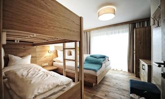 A modern room with a bunk bed and a single bed.  
Large windows let in a lot of light and the wooden floor creates a cozy atmosphere.