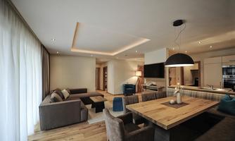A modern living room with a cozy seating area and a large dining table. The room design is bright and inviting, with wooden flooring and soft lighting.