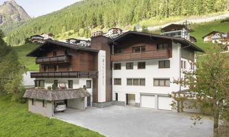 A modern building in a rural setting with mountains in the background. The house has several floors and is surrounded by green landscape.