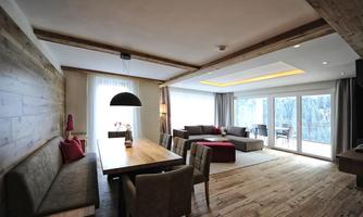 A modern living room with wooden floors and large windows. The space is bright and inviting, with a dining table and cozy seating.