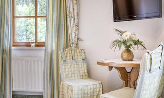A cozy room with a table and two chairs. The window is decorated with colorful curtains, and a TV is mounted on the wall.