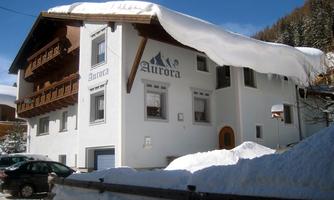 A charming building named "Aurora" with a large snow pile on the roof. The surroundings are snow-covered, perfect for winter activities.